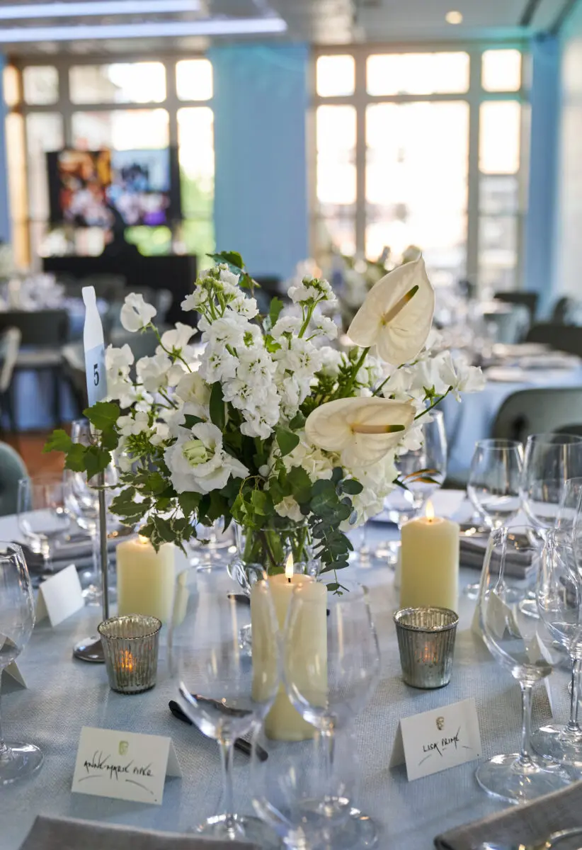 A bouquet of white flowers sits in the middle of a table, surrounded by candles and wine glasses.