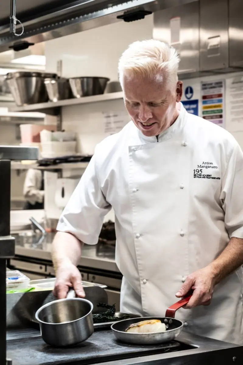 A tall man with white hair in a chef's jacket.