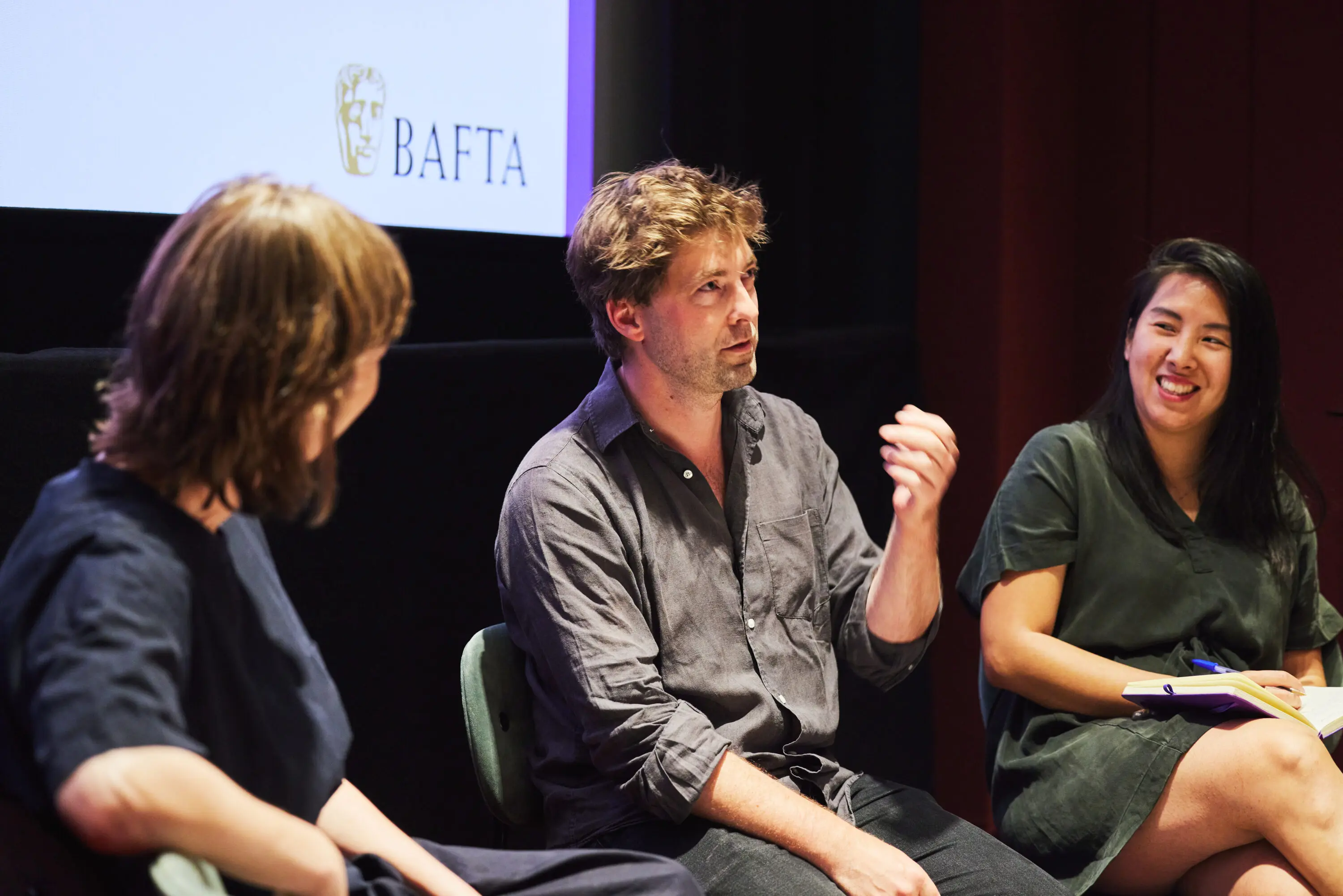 A man in a grey shirt and with short brown hair delivering a talk on stage.