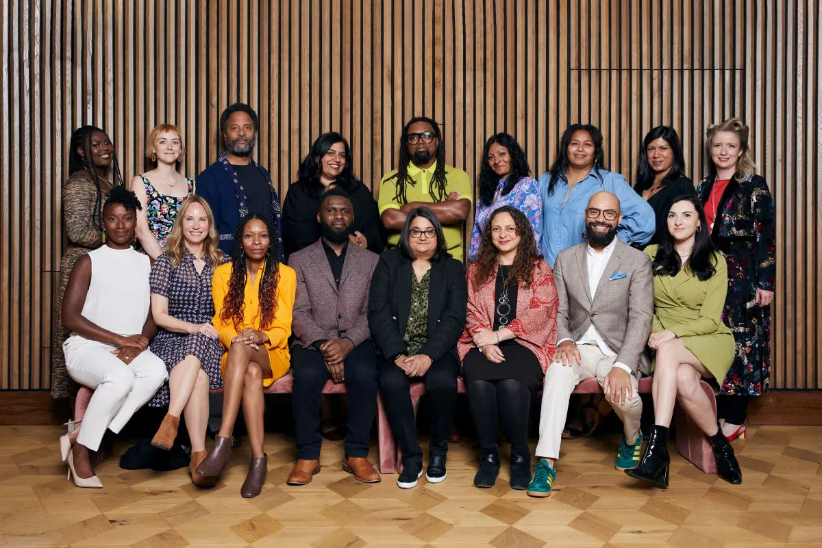 The 2022 Elevate cohort pose together in front of a wood panelled wall.