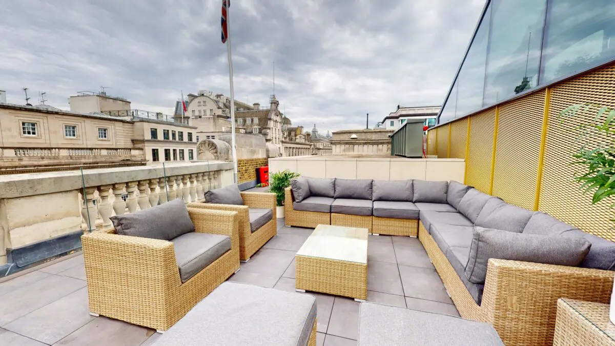 A rooftop terrace with large rattan sofas and grey cushions.