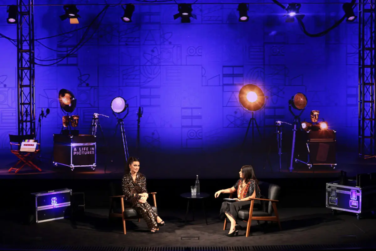 Two women sat on a stage surrounded by spotlights.