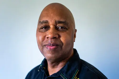 A bald black man wearing a denim shirt with colourful stitching.