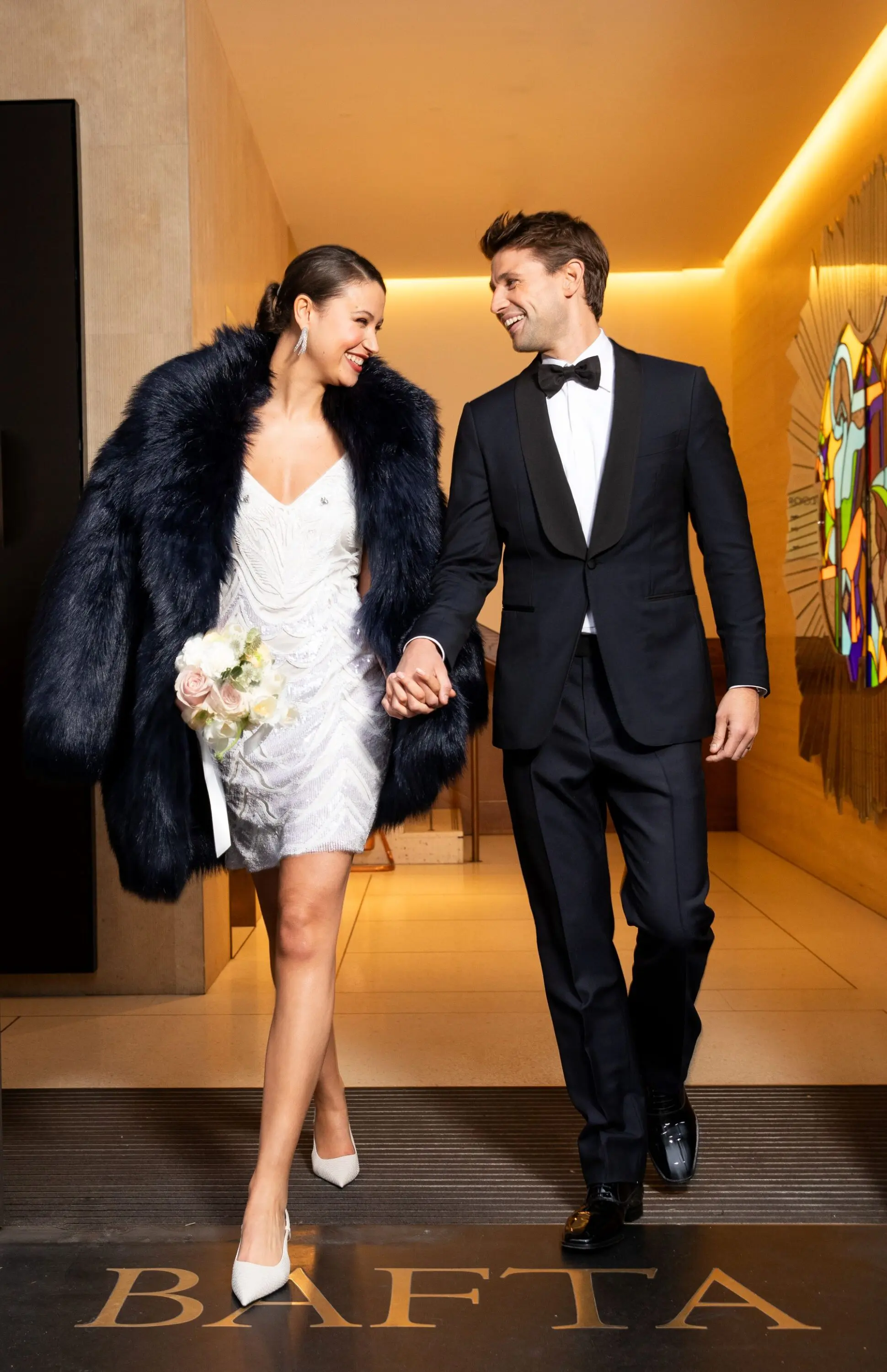 A wedding couple posing walking through the doors of the BAFTA 195 building.