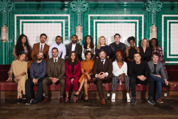 Nineteen of the 2019 Elevate cohort sat in two rows posing for the camera. There is a wall of green and white tiles behind them.