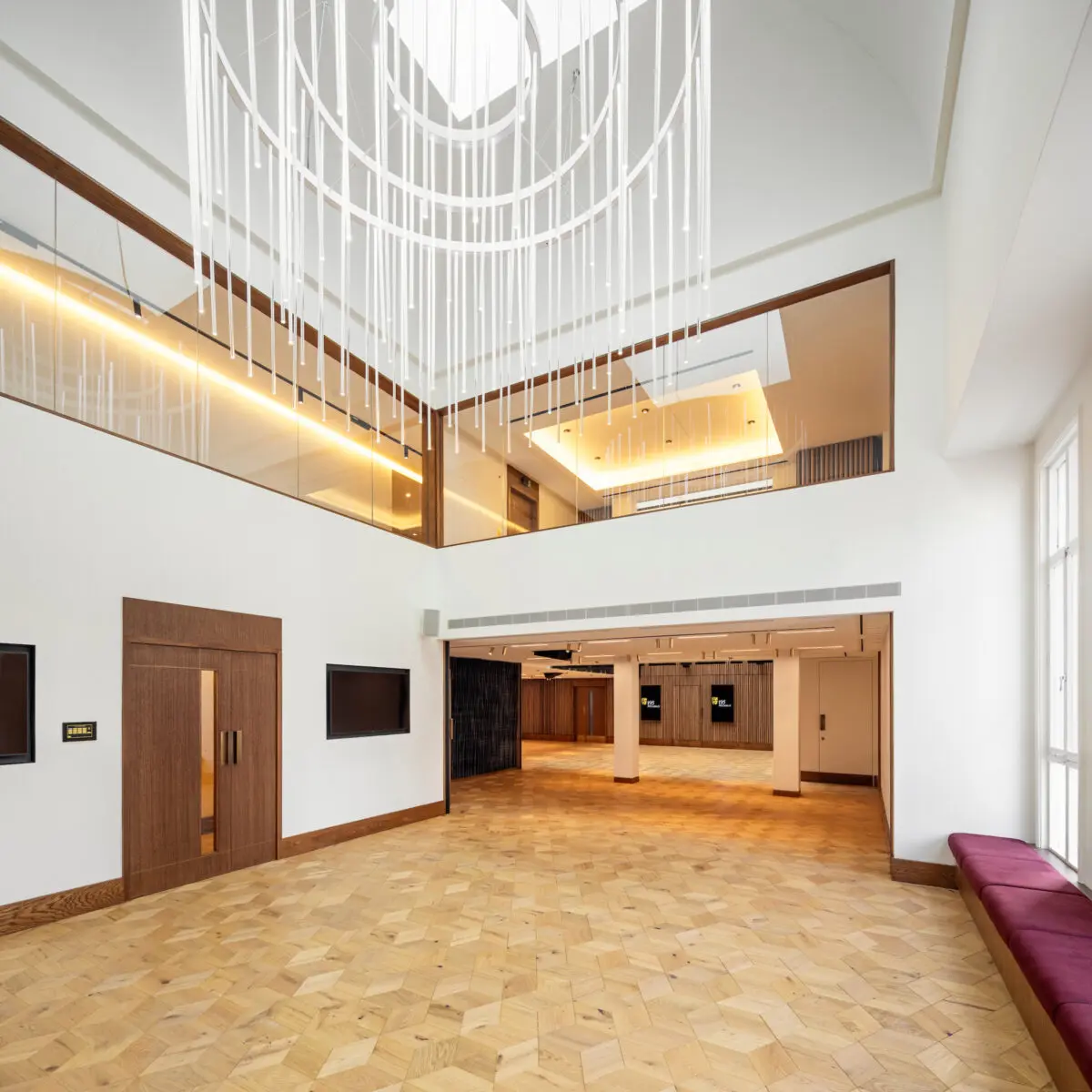 A large open plan room with parquet flooring and a large glass drop chandelier.
