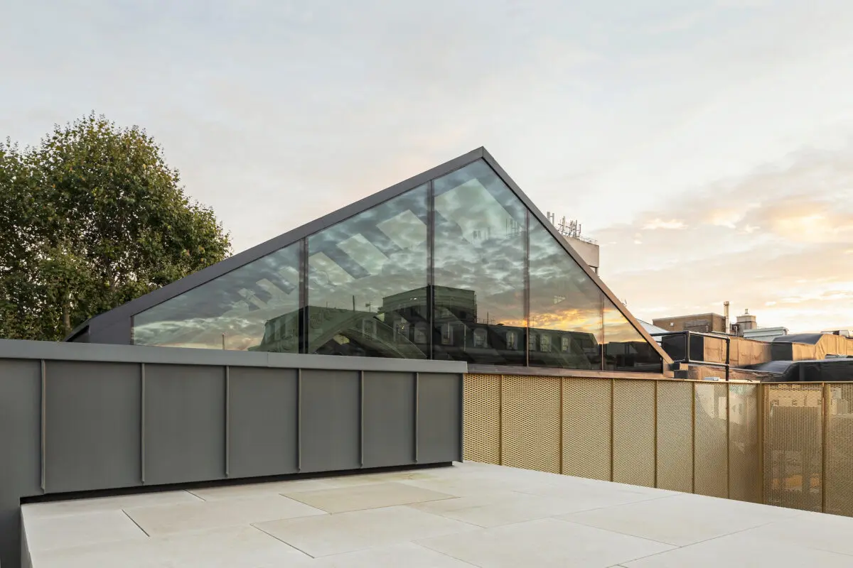 A roof terrace bordered by grey and gold metal barriers and with the top of a glass roof in the background.