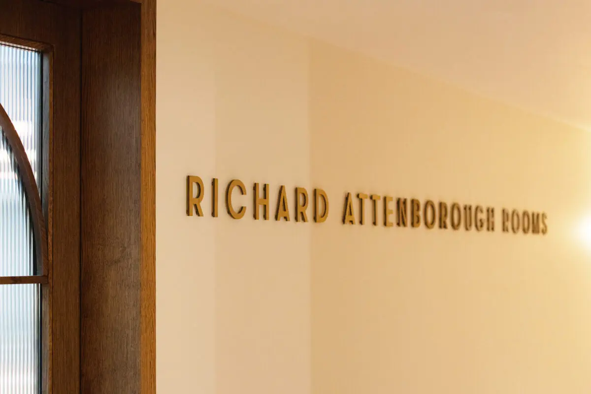 An off-white coloured wall with the words Richard Attenborough Rooms stuck on it.