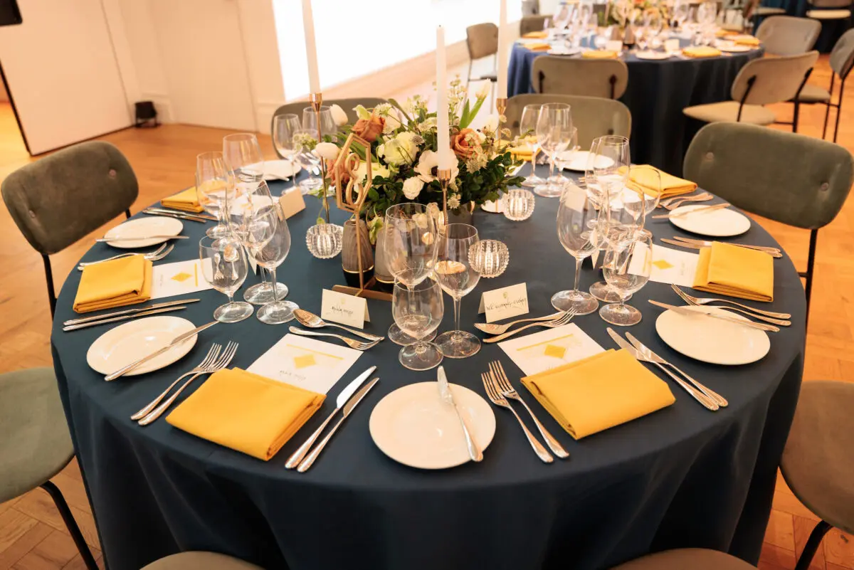 Around table with a blue table cloth laid out for a formal dinner.