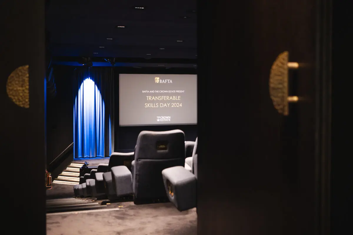 A large door with a gold half circle door handle opening up into an empty cinema. On the screen are the words Transferable Skills Day 2024.