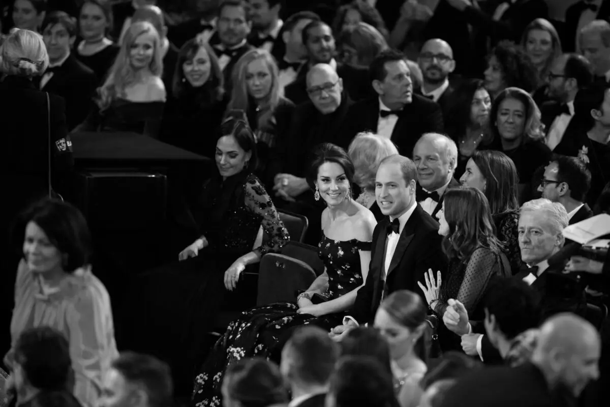 A black and white image of an audience with a focus on a man and woman in the middle. The couple are HRH The Duke and Duchess of Cambridge.