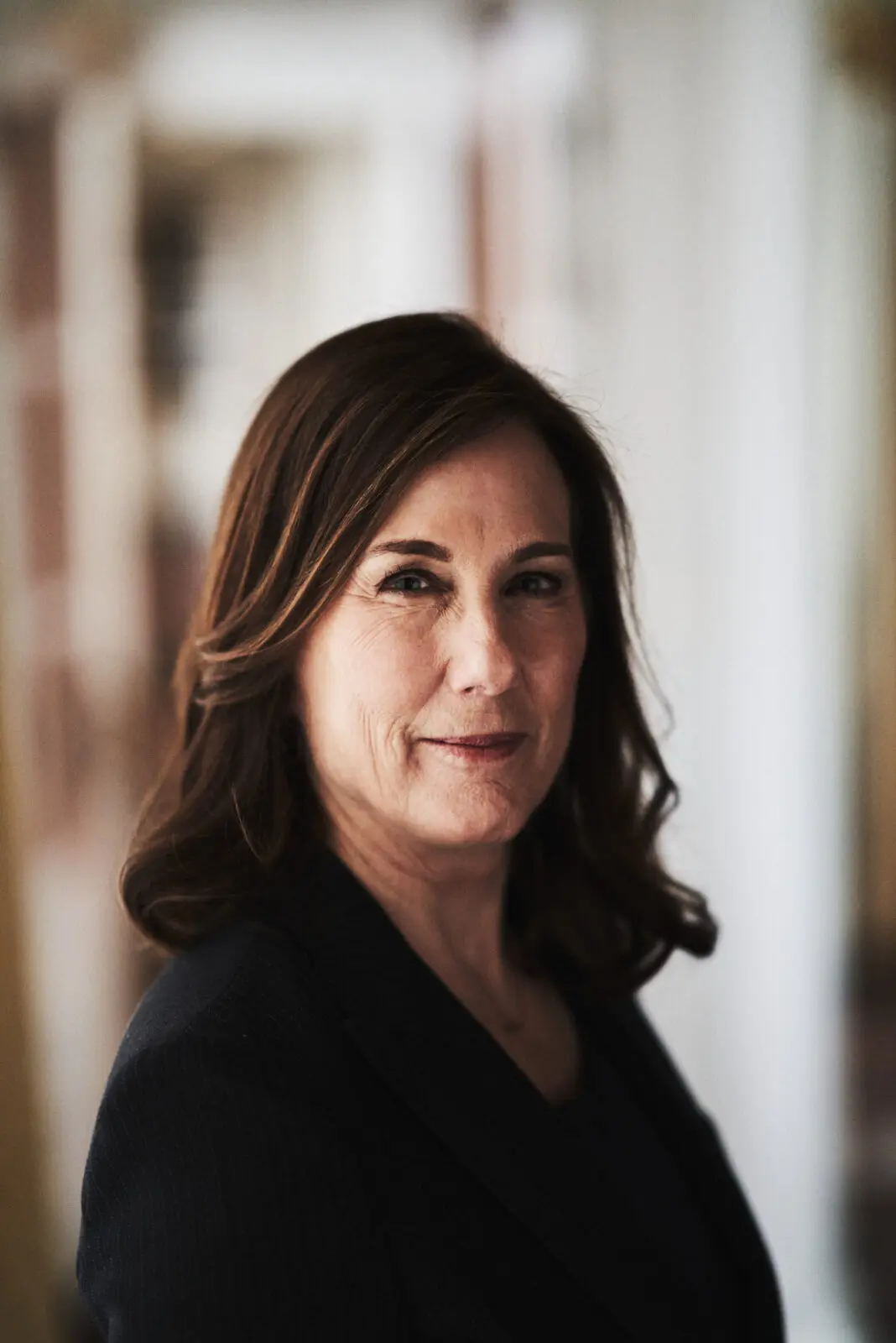 A white woman with shoulder-length dark hair. She is wearing a dark top and facing the camera side on.