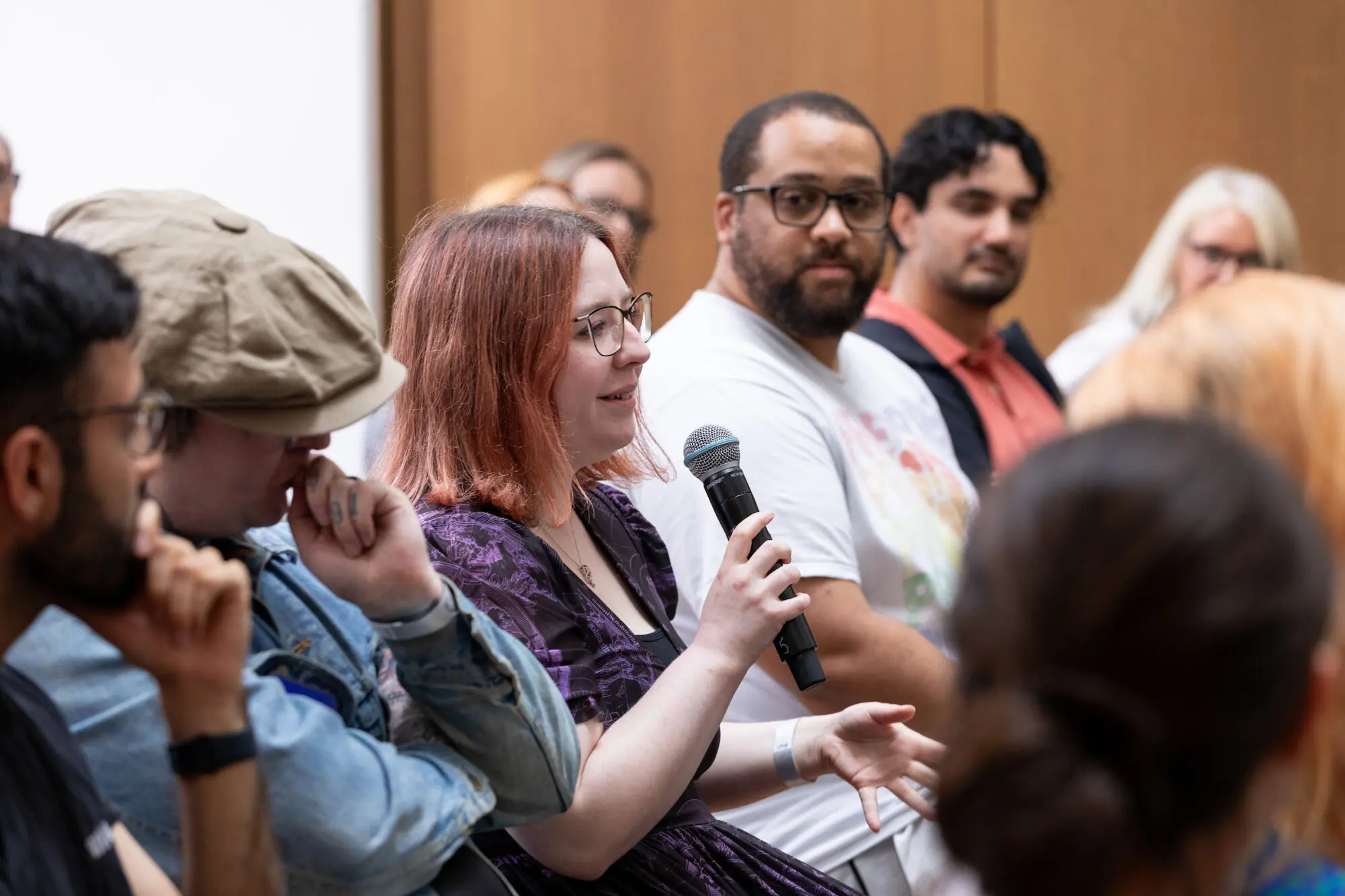 A woman with dyed pink hair speaking into a microphone surrounded by other audience members.