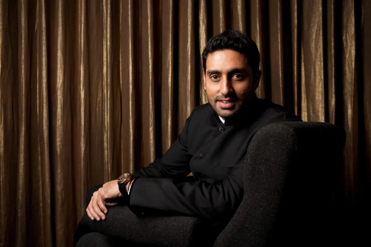 Abhishek Bachchan. A man with black hair and stubble wearing a black suit sat in a large black armchair.
