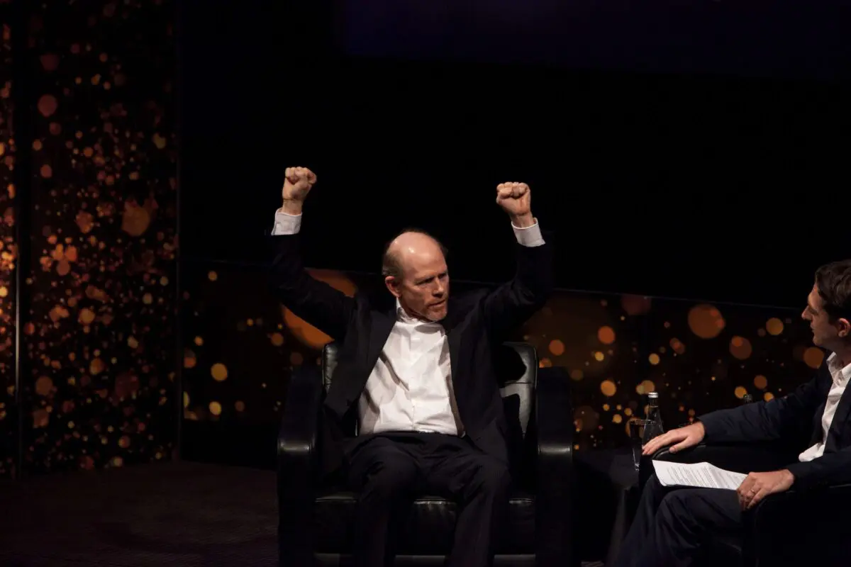 Ron Howard. A man with short hair on the sides and bald on top, sat on stage wearing a white shirt and black suit.