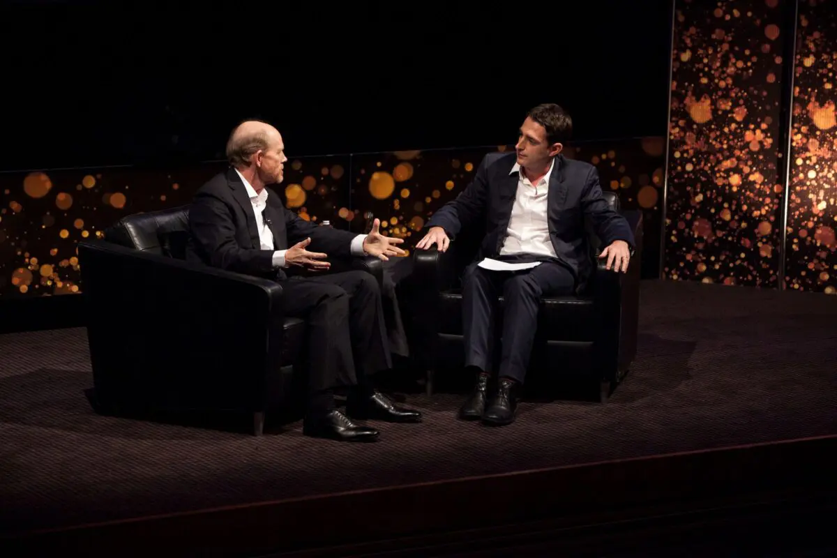 Ron Howard. A man with short hair on the sides and bald on top, sat on stage wearing a white shirt and black suit.