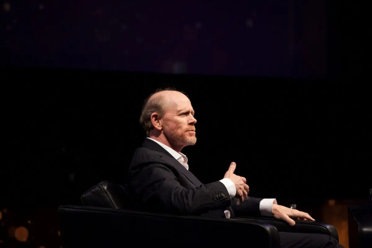 Ron Howard. A man with short hair on the sides and bald on top, sat on stage wearing a white shirt and black suit.