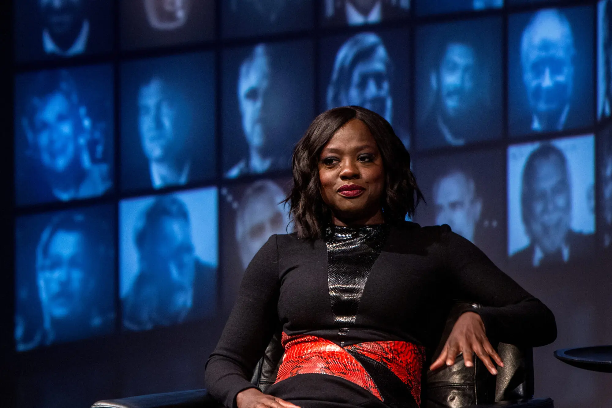 Viola Davis. A black woman with black bobbed hair wearing a black top with red statement belt.