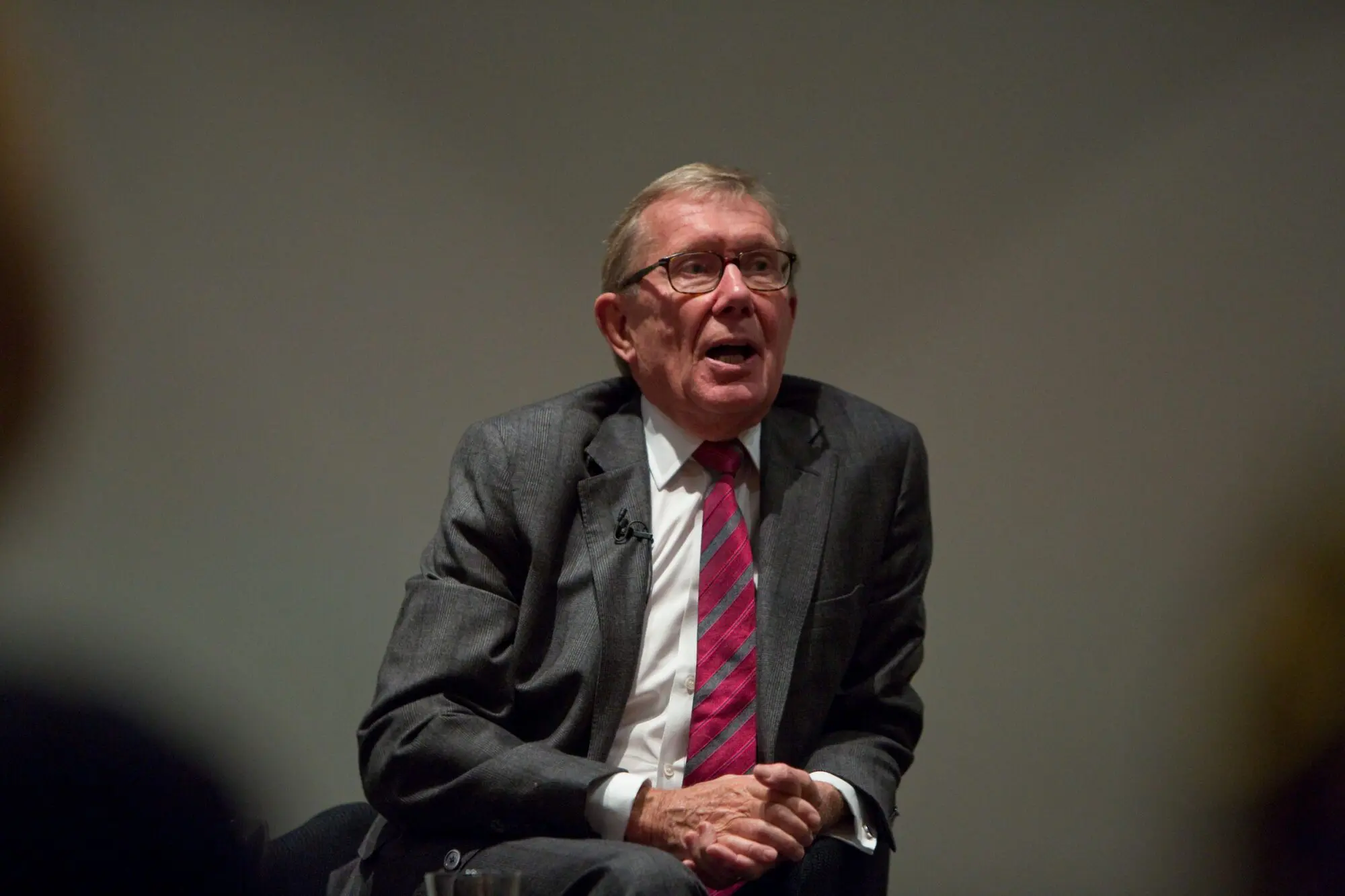 Jonathan Birch. A white man with white hair and glasses wearing a white shirt, red tie and grey suit.