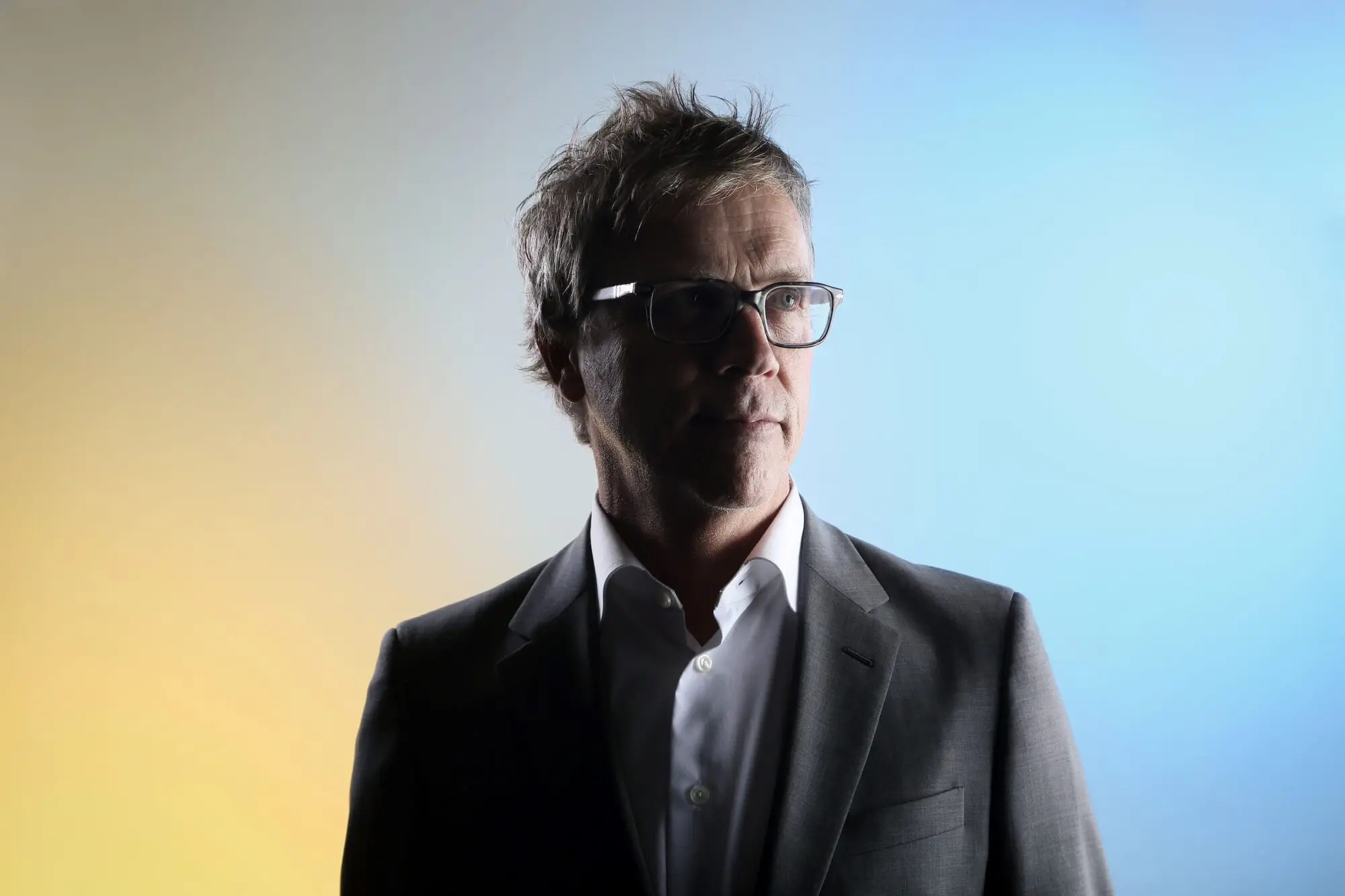 Todd Haynes. A white man with short dark brown hair wearing thick black rimmed glasses, a white shirt and grey blazer.