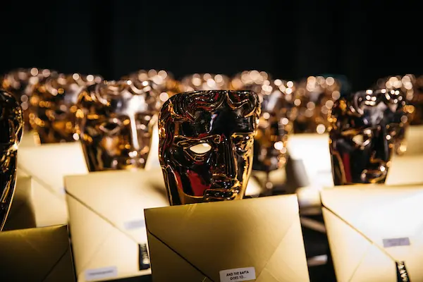 Rows of BAFTA masks in a dark room with golden envelopes leaning against them.