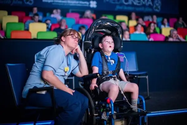 A young boy in an accessible pram watching a screen with a nurse sat next to him.