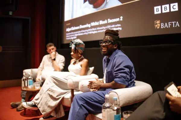 Two men and a woman sat in large grey armchairs addressing an audience.