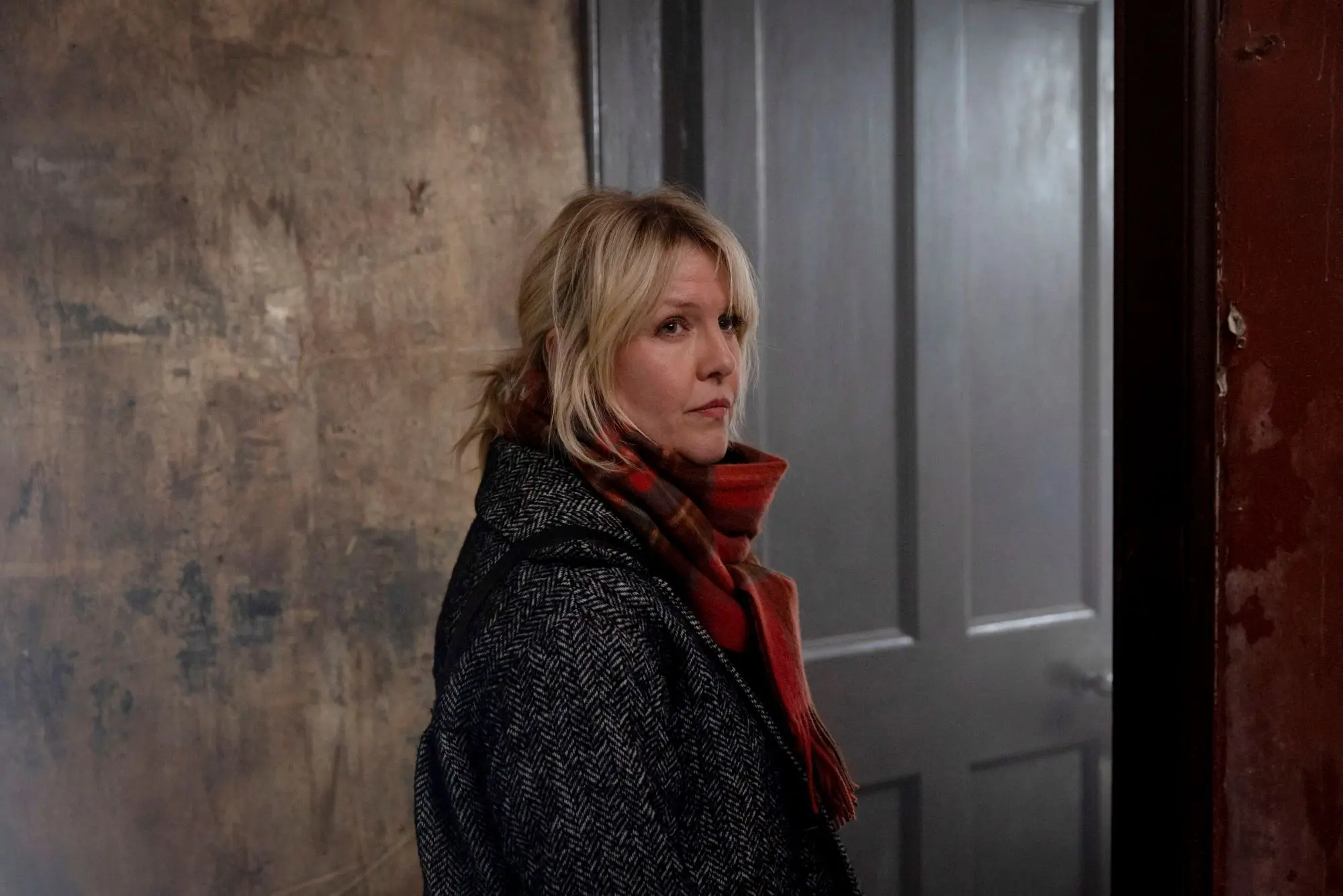 A still of Ashley Jensen in Shetland. A woman with short blonde hair tied in a low ponytail wearing a thick wool coat and red scarf.