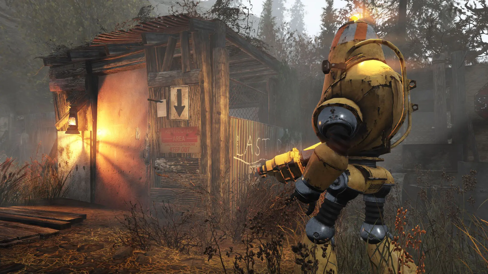 A still from the game Fallout 76. A figure in what looks like a yellow metal suit approaching a ramshackle wood hut.
