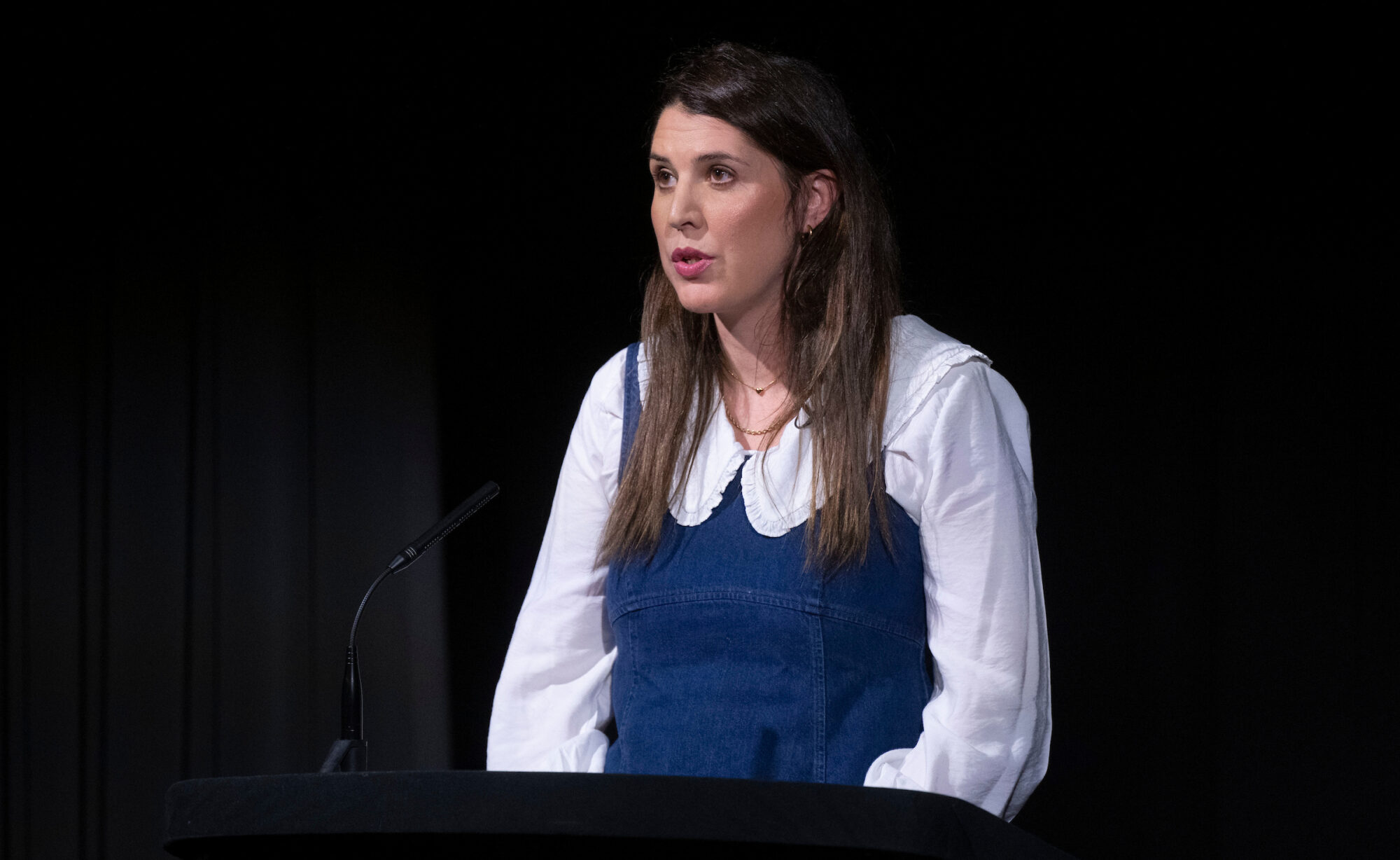 Alice Birch. A woman with long brown hair wearing a white shirt with large collar under a blue denim pinafore.